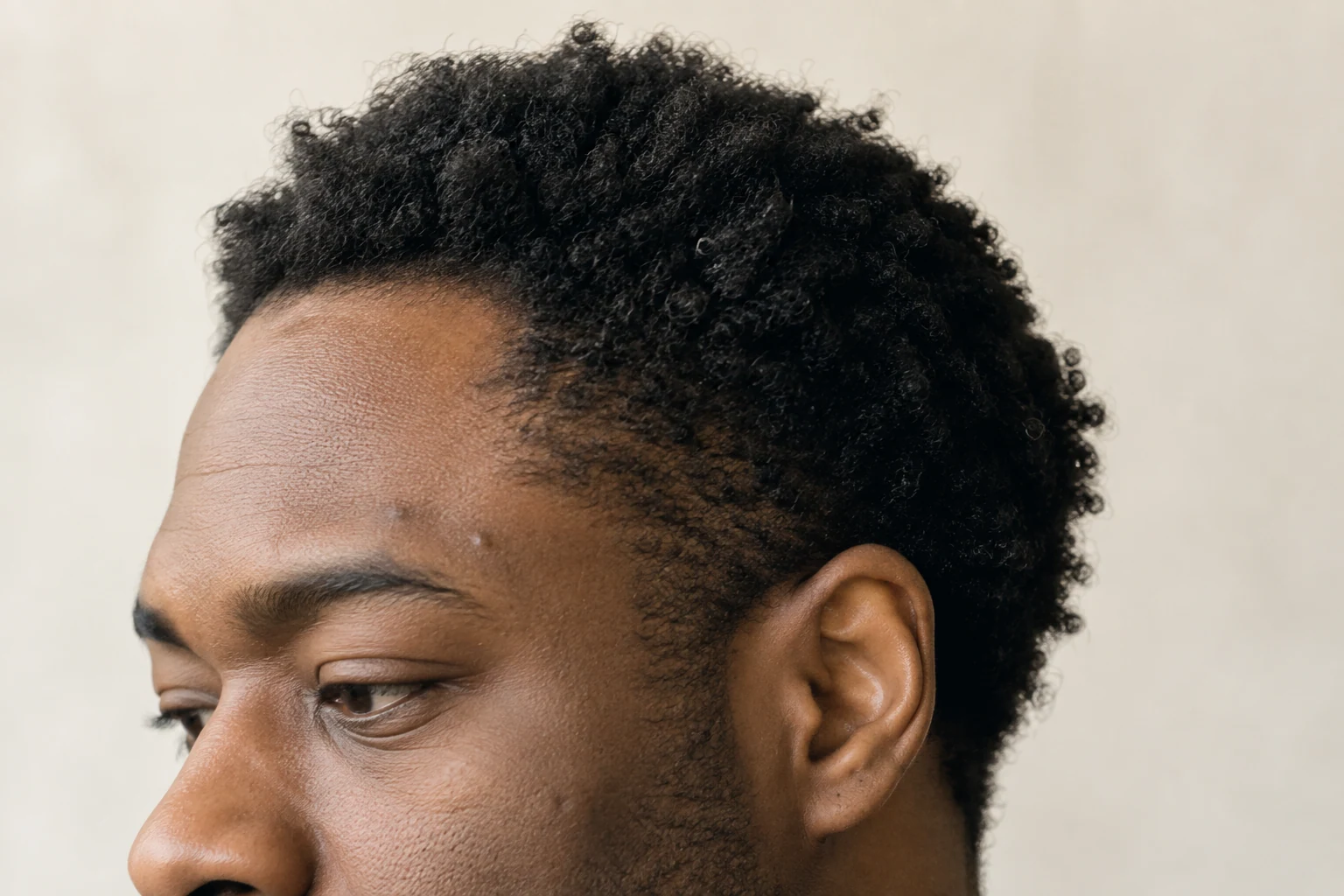 Retrato próximo de homem negro com cabelo crespo natural, poros, pequenas marcas e fios soltos.